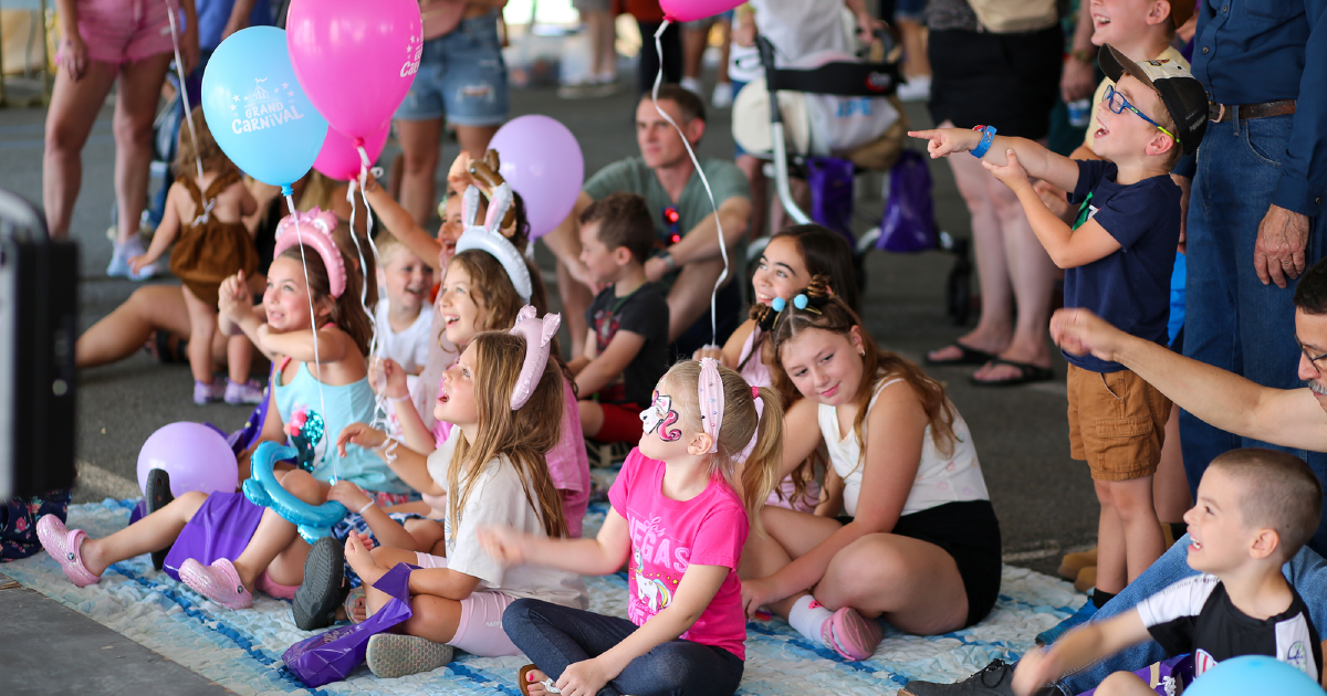 Children with balloons watching a magic show at the Pioneer Grand Carnival